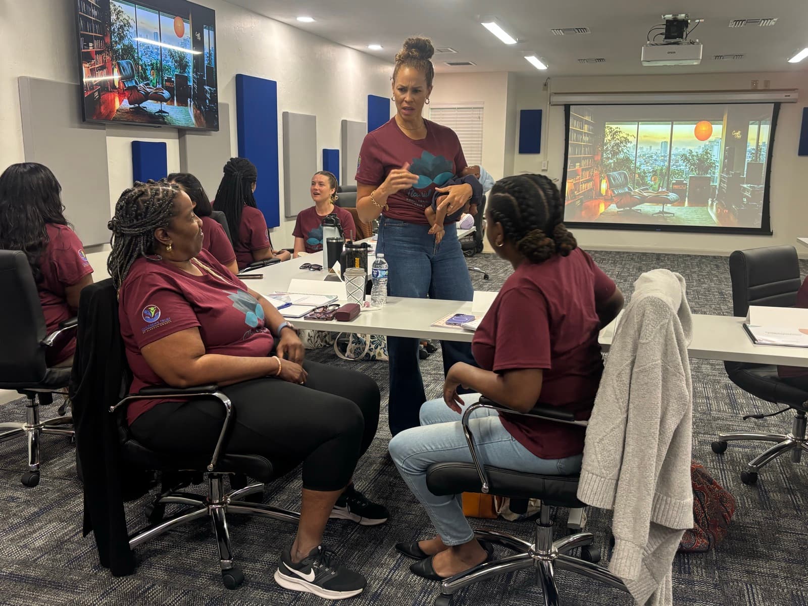A trainer leads a small-group discussion with doula trainees seated around a classroom table