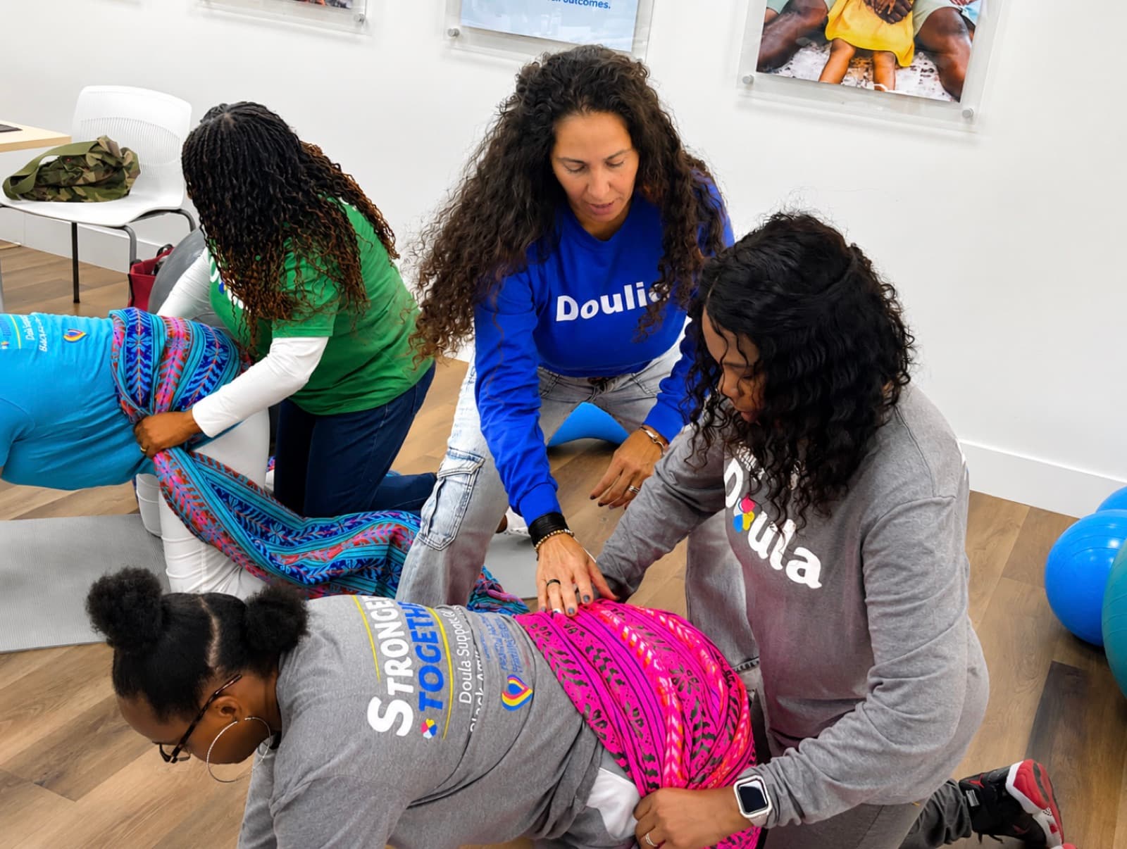 A trainer in a Doulio shirt guides doulas as they practice a hands-on comfort technique with a rebozo